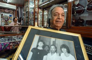 24 Mar 2003, India --- Bishan Dass runs the sitar store with his son Ajay (in the background). Here, he proudly shows a photo taken in 1966 with 2 members of The Beatles, Paul McCartney, George Harrison and himself.  Rikki Rama's father started the business over 80 years ago in Lahore, in what is today, Pakistan. With the arrival of partition in 1947, they left for Delhi and the store has been in Connaught Circus ever since.